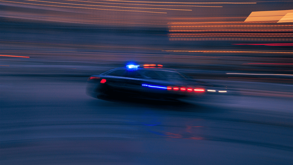  A police car speeds down a street at night in a film scene that will use royalty free siren sound effects in the sound design