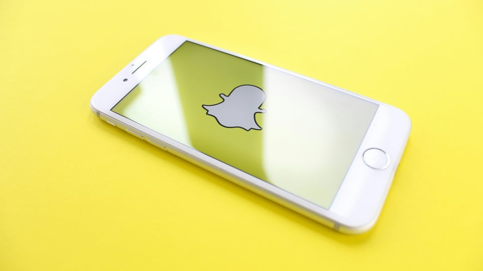  A smartphone on a yellow background loads the Snapchat app, getting ready to add royalty free music for Snapchat to video snaps.
