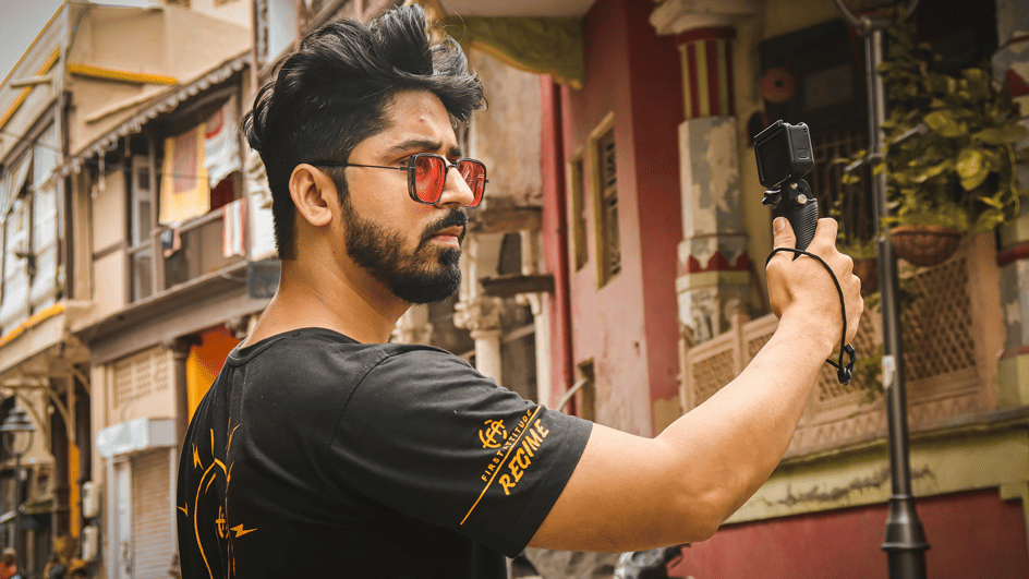  A man holds up a camera, shooting footage for his vlog, as he ponders where to find the best royalty free vlog sound effects download.