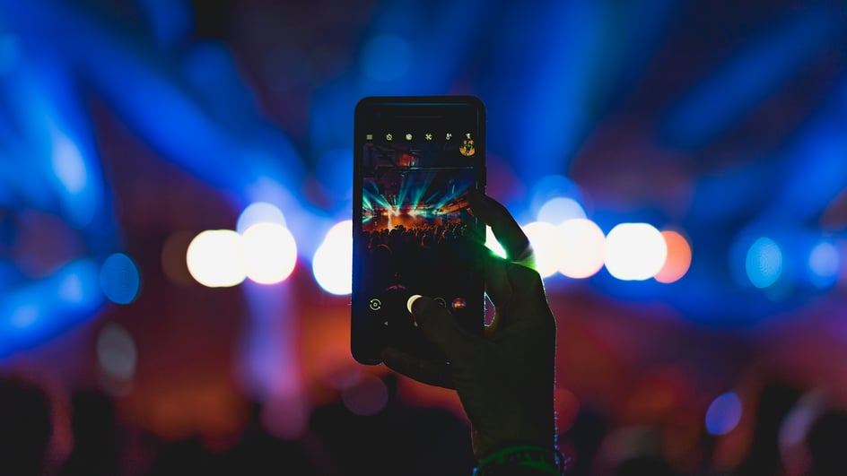  A hand holds up a smartphone, recording a clip from a live concert, as the content creator wonders, how to add music to YouTube Shorts?