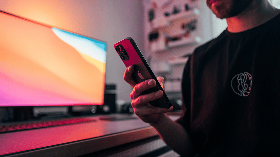  A man sits next to his edit suite, searching on his phone about how to grow on YouTube Shorts.