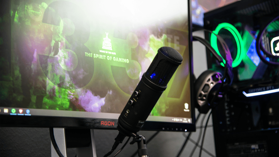  A black microphone stands next to a gaming pc, recording royalty free gaming music.
