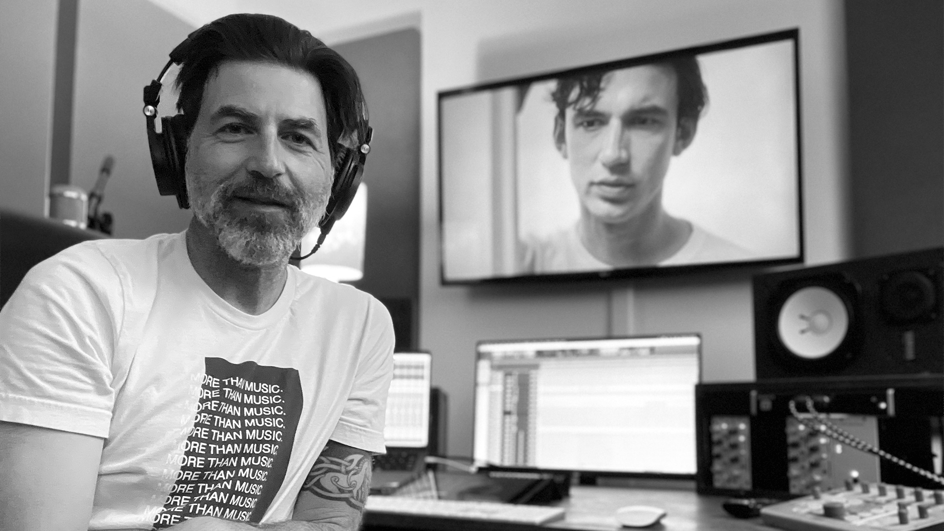  Adrian Walther sits at his keyboard, headphones on, recording royalty free soundtrack music for video.