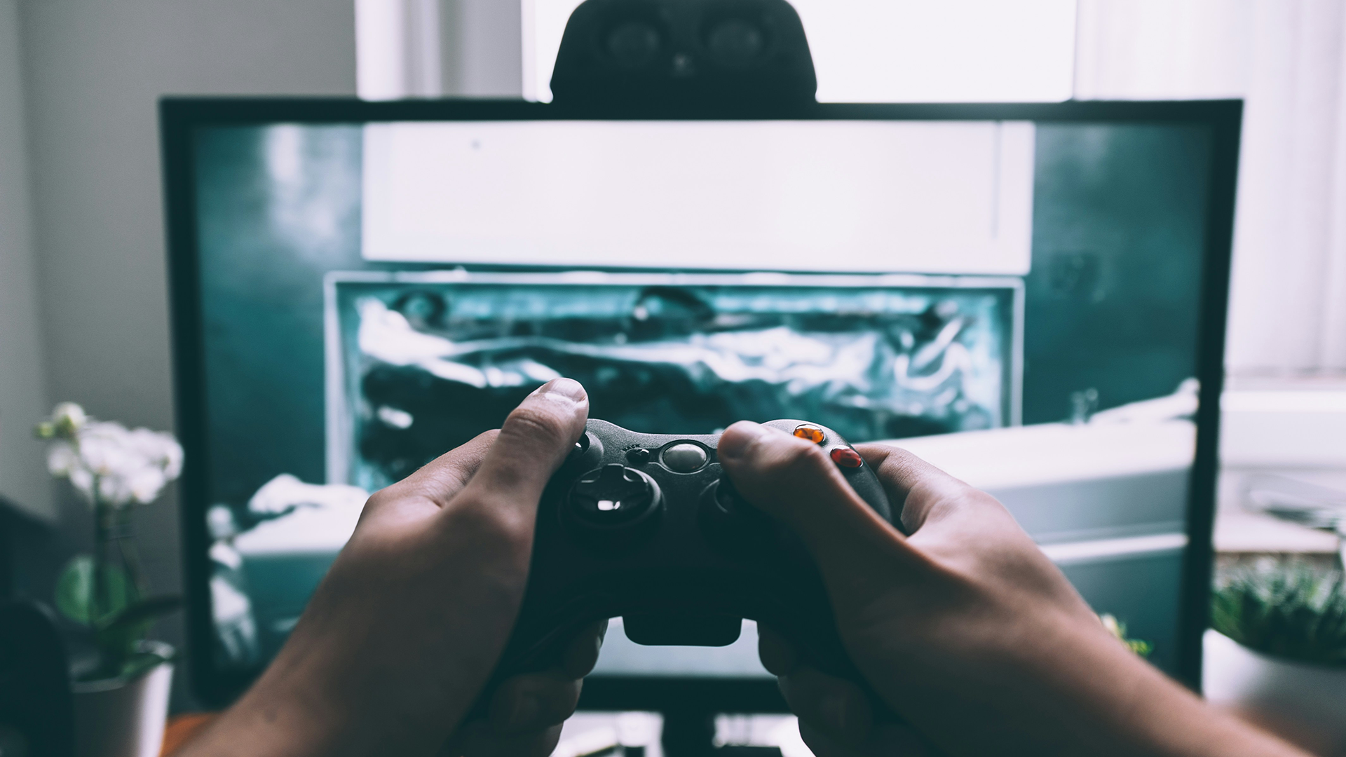 A person holds a game controller in front of a game they created while considering the perfect video game music licensing option.